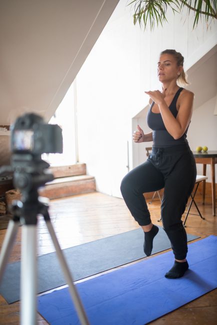 Woman performing exercises at home while recording an online workout video in a bright living room.