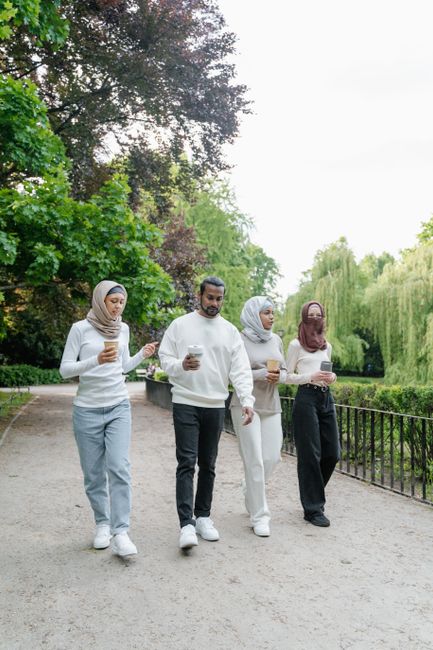 Four friends sipping coffee and walking through a park together in casual attire.