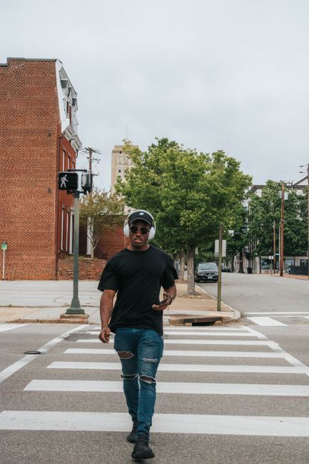 Man walking confidently across a city crosswalk with headphones and casual attire.