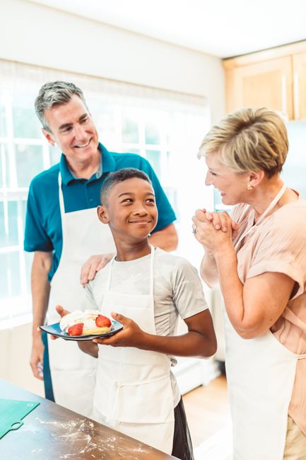 A joyful family with an adopted child cooking together in a bright kitchen, wearing aprons and smiling.