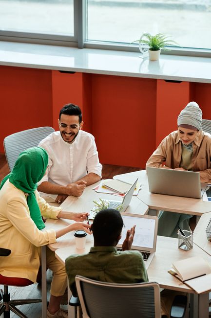 A diverse team having a meeting in a bright office space, discussing ideas and using laptops.