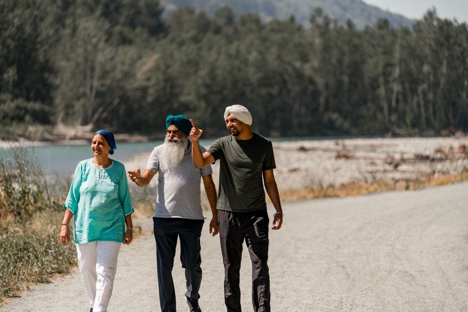 Three adults walking on a serene forest trail by the river during a sunny day.