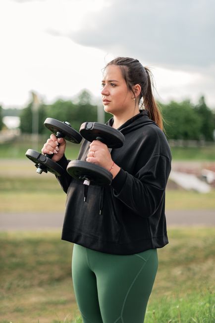 Woman in active wear lifting dumbbells outdoors, promoting fitness and wellness.