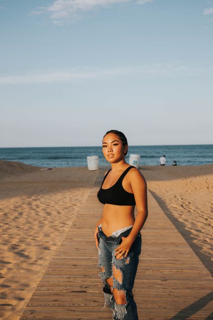 Confident woman in ripped jeans and sports bra on a sunny beach boardwalk.