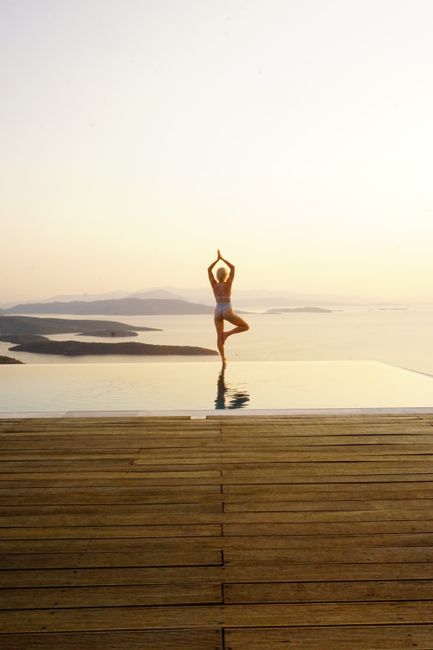 Woman practicing yoga on a pier at sunrise, overlooking a serene sea in Greece.