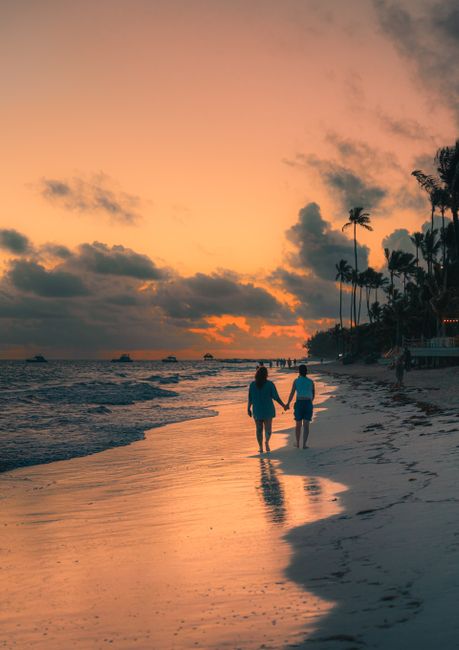 Couple walking hand-in-hand along a tropical beach at sunset, creating a romantic ambiance.
