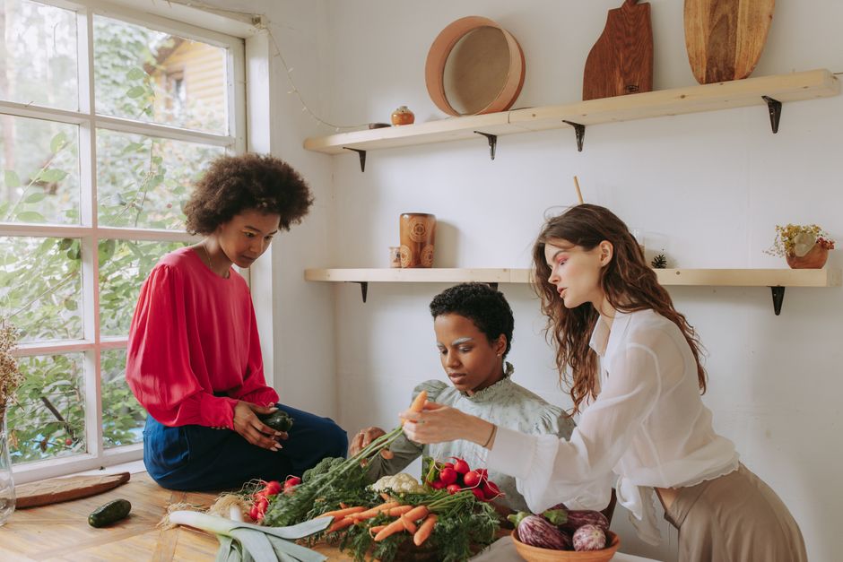 Three women enjoying a cooking session with fresh vegetables in a bright kitchen.