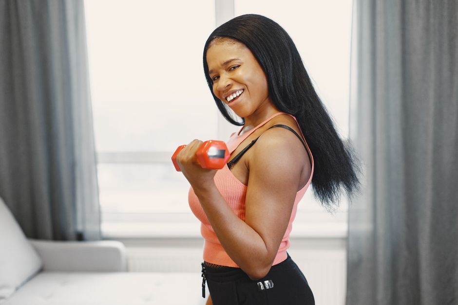 Fit woman smiling while lifting dumbbell, exercising at home. Bright and energetic atmosphere.