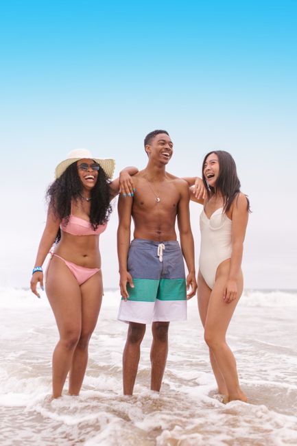 Three friends laughing and having fun at the beach in summer swimwear.