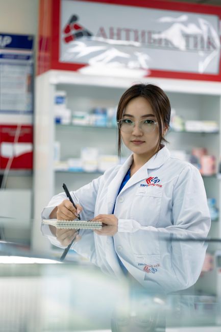 Female pharmacist writing in notepad inside a pharmacy.