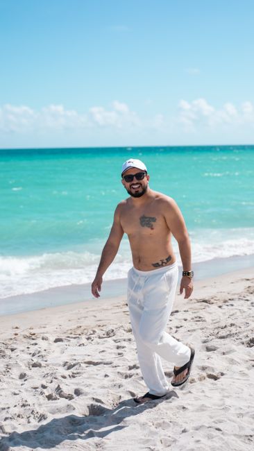 Shirtless man walking along a sunny beach, enjoying the summer day with clear blue skies.