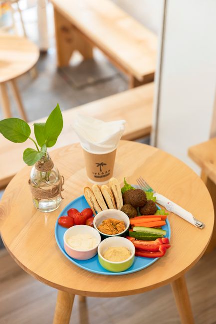 A colorful Middle Eastern breakfast featuring falafel, dips, and coffee on a wooden table.
