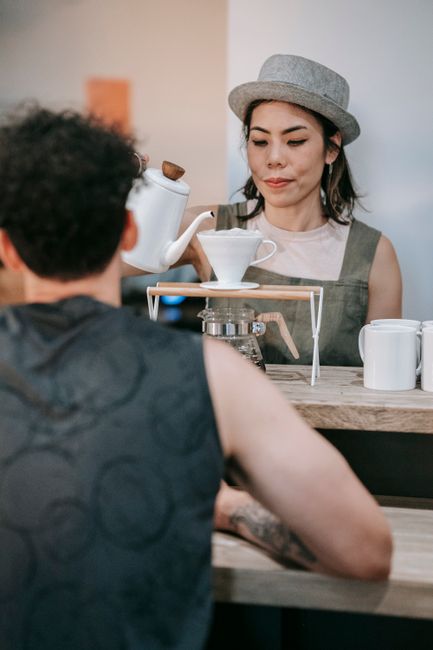 Barista skillfully pours coffee in a modern cafe setting, engaging with a customer.