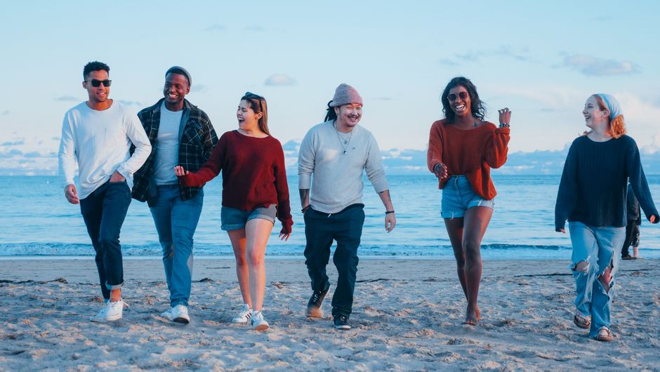 A diverse group of friends happily walking on the beach during sunset, embracing friendship and leisure.