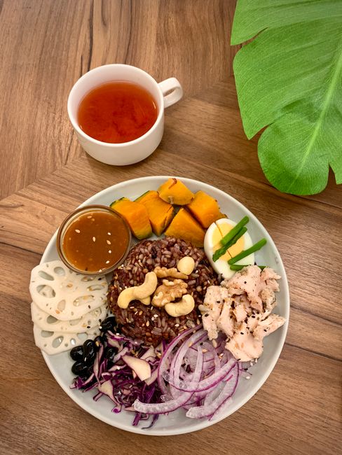 Colorful healthy meal featuring vegetables, rice, nuts, and tea on a wooden table.