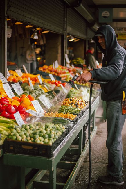 Man in black hoodie washing fresh vegetables at a market stall, maintaining cleanliness and appeal.