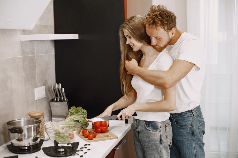A loving couple enjoys cooking fresh vegetables together in a cozy, modern kitchen setting.