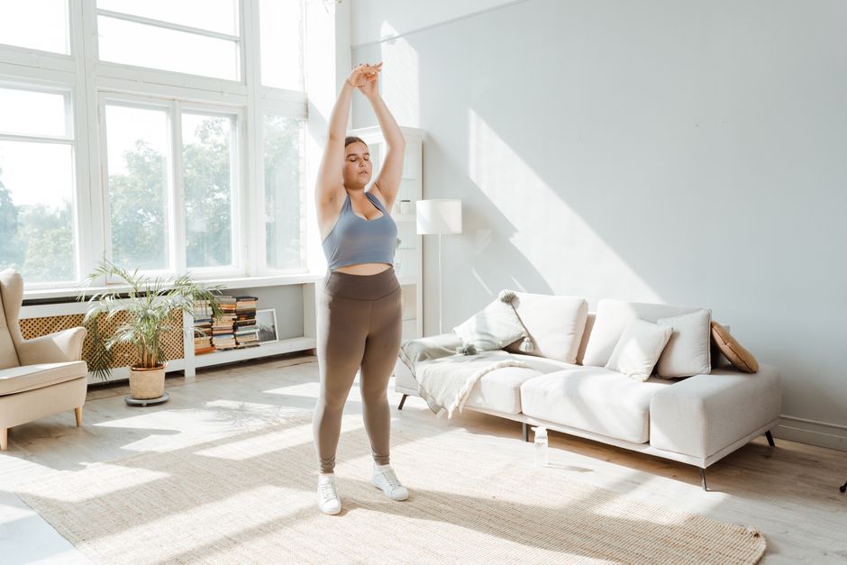 Woman in activewear stretching in a bright living room, embracing a healthy lifestyle.