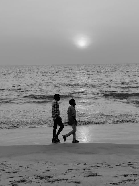 Two individuals walk along the beach in silhouette during a tranquil sunset, creating a serene coastal scene.