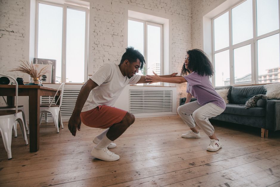 An interracial couple exercising together at home in a bright, modern living room.