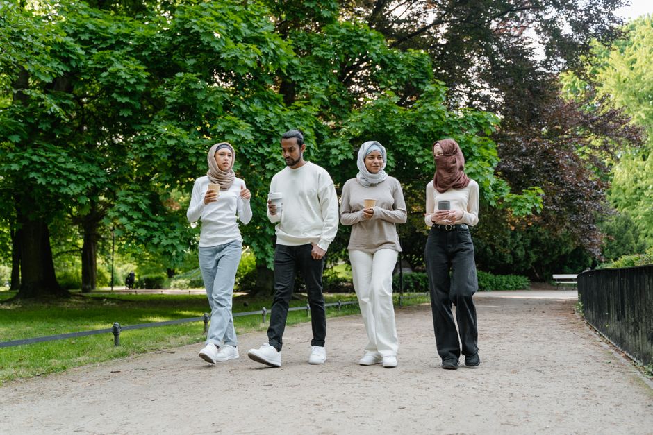 Group of diverse friends walking in a park, holding coffee cups and enjoying a sunny day outdoors.