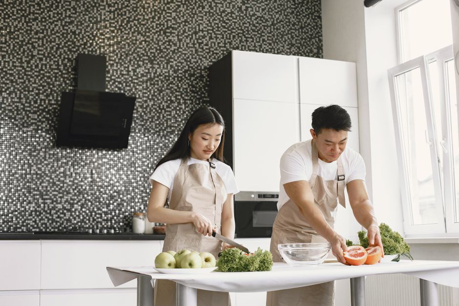 Asian couple slicing vegetables in a modern kitchen setting, showcasing home cooking together.