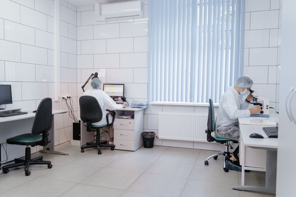 Two laboratory technicians working with computers and microscopes in a clean, modern lab.