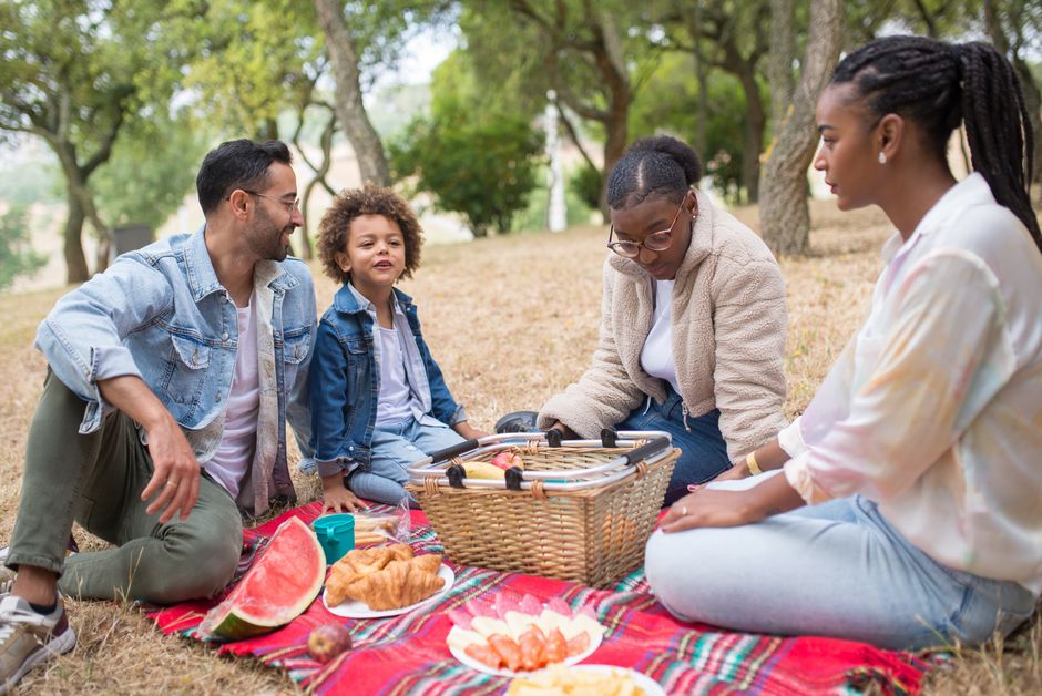 A diverse family enjoying a picnic on a sunny day outdoors in Portugal, featuring watermelon and croissants.