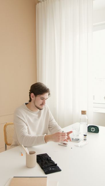 A man checks his blood glucose levels using a glucometer in a bright room.