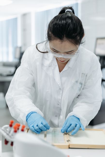 A female scientist examines samples in a laboratory setting, wearing protective gear.