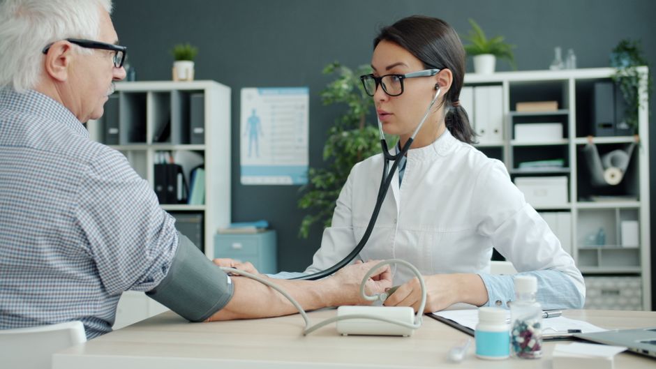 Healthcare professional checks senior's blood pressure at clinic for health assessment.