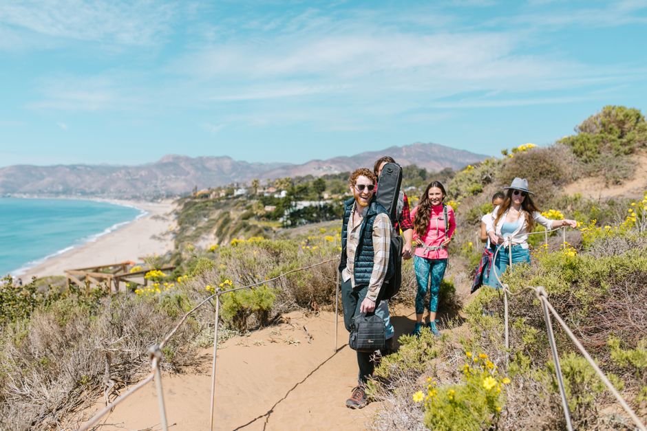 Group of friends hiking on a sunny day along a scenic coastal trail with ocean views.