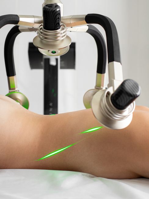 Crop anonymous topless female patient lying under green lasers of modern fat loss machine with heads in light medical clinic