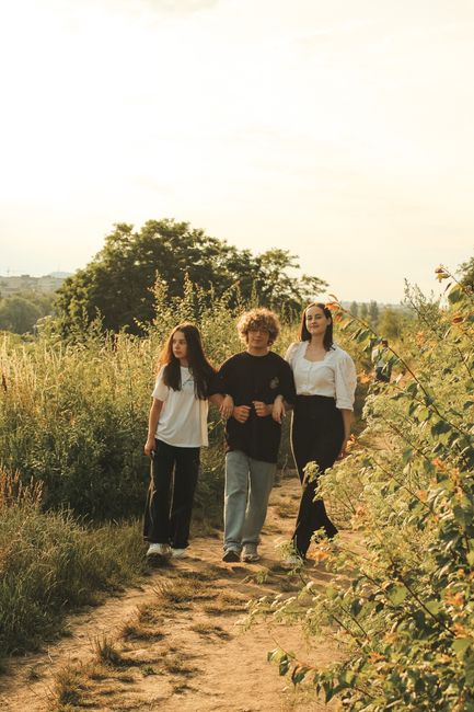 Three friends walking on a dirt path surrounded by lush greenery on a bright sunny day.