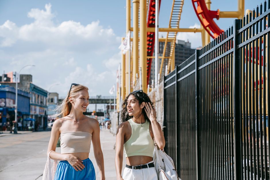 Two friends walking and talking at an amusement park on a sunny day, enjoying their time together.