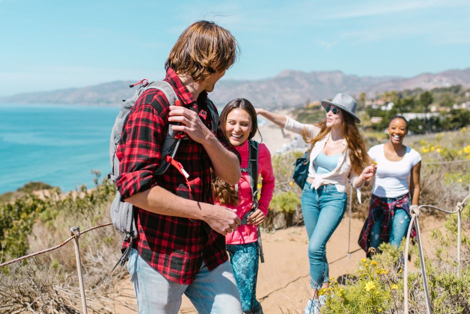 Laughing group of friends hiking on a scenic coastal trail with sunny views.