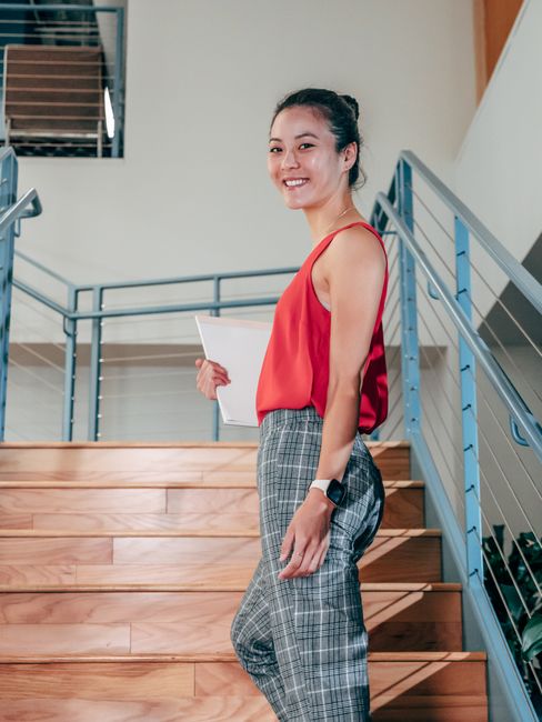 Smiling woman in a red top climbing stairs, representing professional confidence.