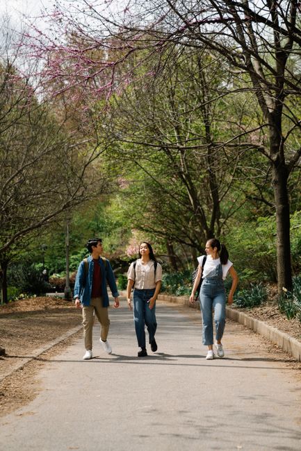 Three friends casually walking on a park path during springtime, enjoying a bright day.