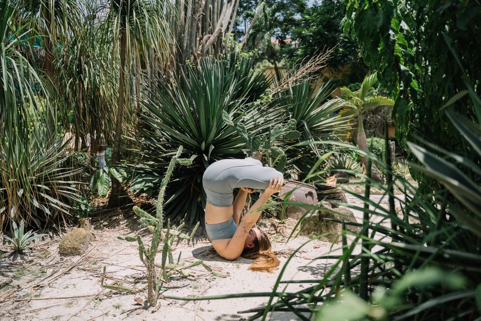 A woman performing a headstand yoga pose outdoors in a vibrant, lush garden setting.