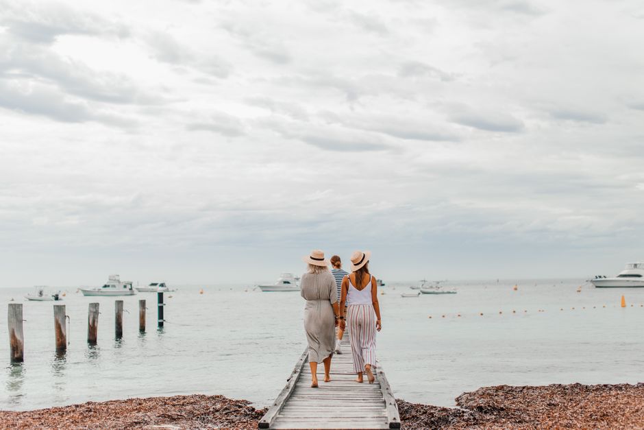 Three friends stroll along a wooden boardwalk at the beach, enjoying a cloudy day by the sea.
