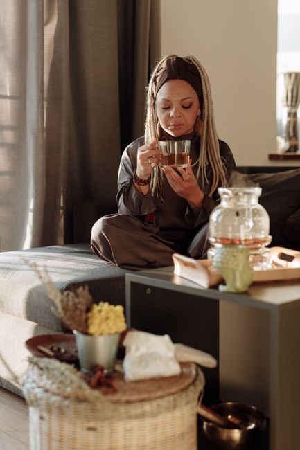 A woman with braided hair relaxes and enjoys a cup of tea in a peaceful living space.