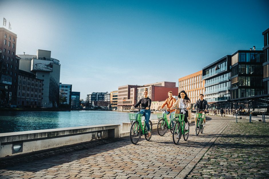 People biking along a canal in a modern urban area under a clear sky.