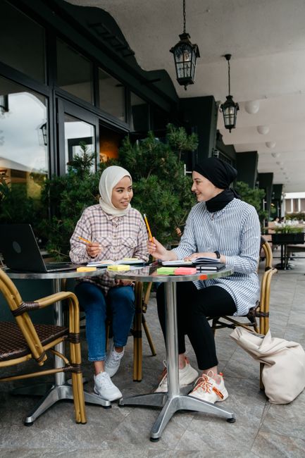 Two women wearing headscarves enjoying a collaborative meeting at an outdoor café.