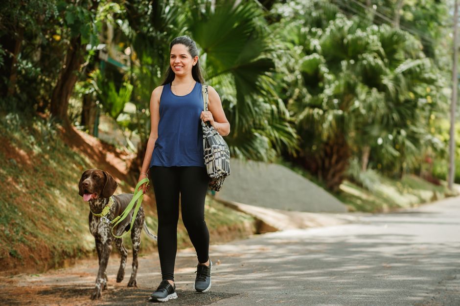 Smiling woman enjoys a sunny walk with her dog in a lush green park.