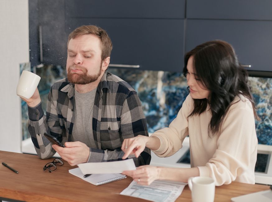 A couple reviews bills at their kitchen table, looking concerned and thoughtful.
