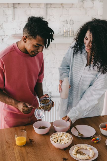 A joyful couple preparing a healthy breakfast with cereals and milk at home.