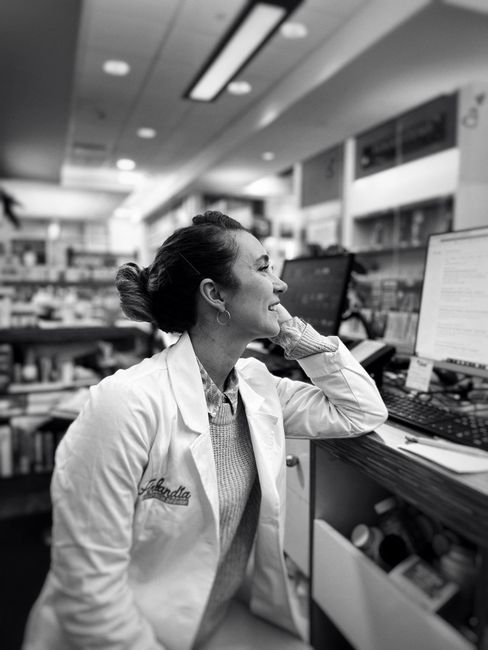 A smiling female pharmacist in a white coat working at a computer in a pharmacy.
