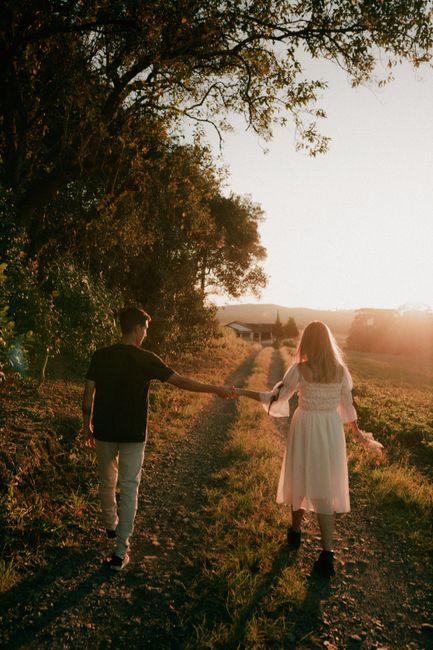 Couple holds hands walking on a countryside path at sunset, in a peaceful autumn setting.