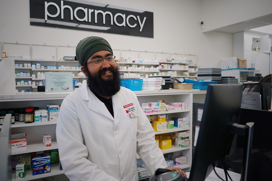 Male pharmacist with a turban standing and smiling in a pharmacy, working at the counter.